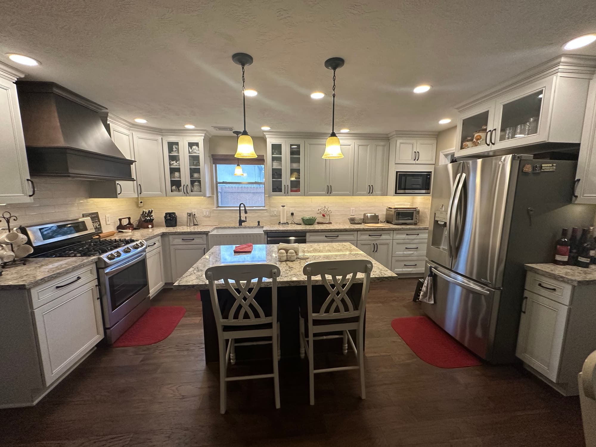 Wide view of the completed kitchen showing a wood range hood, gas range, seated island and hardwood flooring