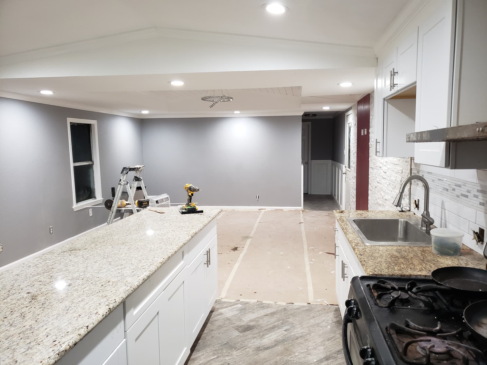 Kitchen nearing completion with white shaker cabinets, granite countertops, a stacked-stone backsplash and freshly painted grey walls